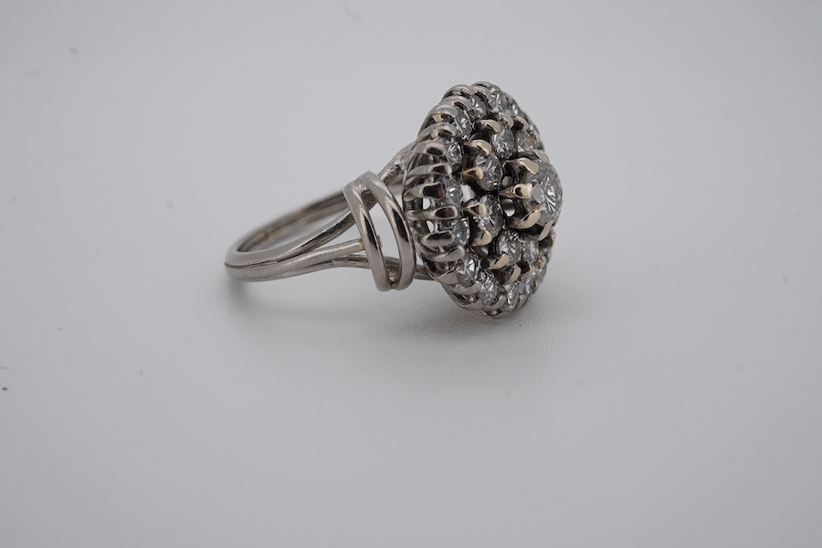 A white metal and diamond cluster set dress ring, with 'wire work' shoulders, size H, gross weight 5.2 grams. Condition - fair to good